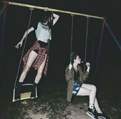 two people are sitting on swings in the dark, one is holding onto another person's leg