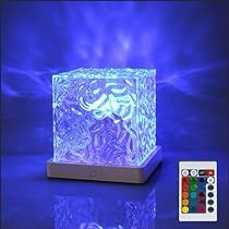 an illuminated cube on a stand with remotes next to it and a blue background