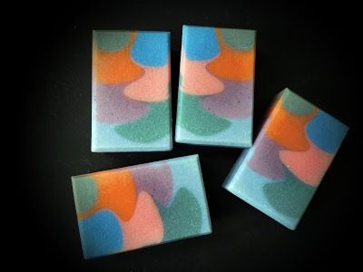 four square coasters with multicolored designs on them sitting on a black surface