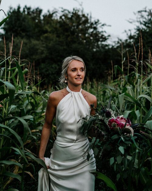 a woman in a white dress holding a bouquet and standing in front of some plants