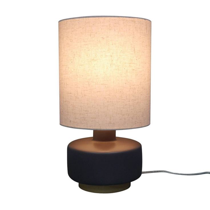 a table lamp with a white shade on it and a cord plugged into the base