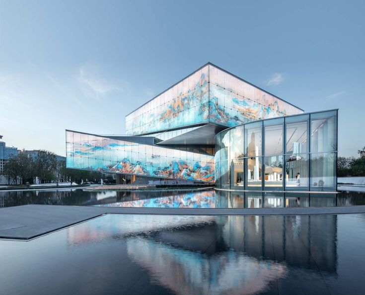 an artistic glass building is shown in the evening light with its reflection on the water