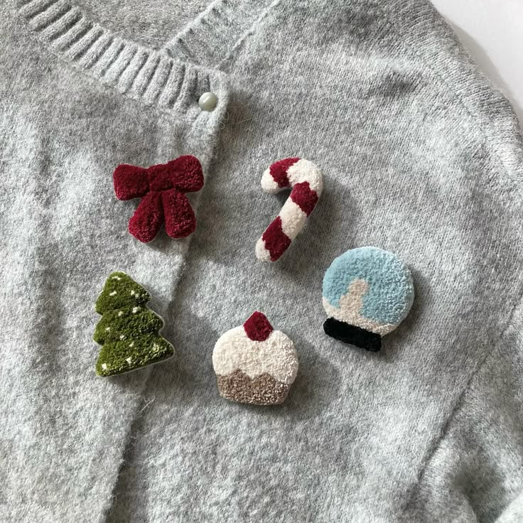 four felt christmas ornaments are placed on top of a gray sweater with red, white and green bows