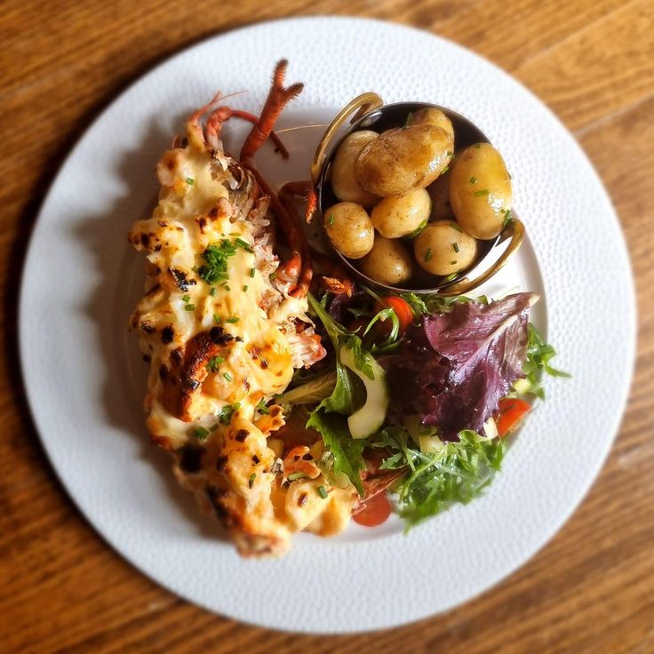 a white plate topped with food next to a bowl of potatoes and veggies