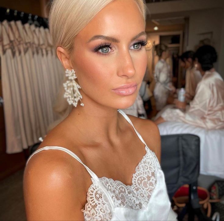 a woman with blonde hair and blue eyes in a white dress looking at the camera