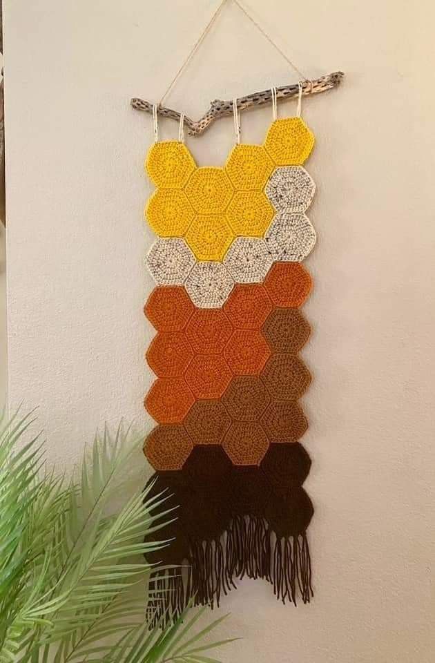 a crocheted wall hanging on the side of a white wall next to a potted plant