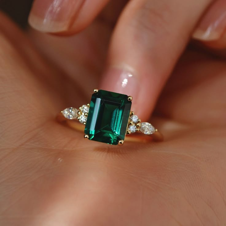 a woman's hand holding an emerald and diamond ring