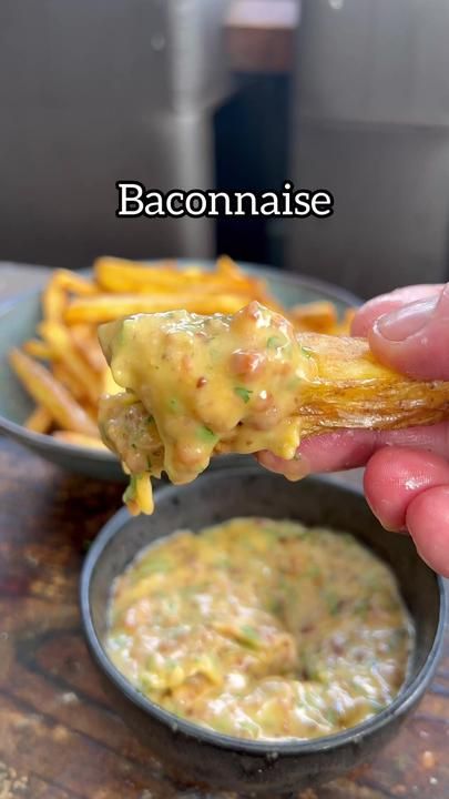 a hand holding up a piece of food with sauce on it and french fries in the background