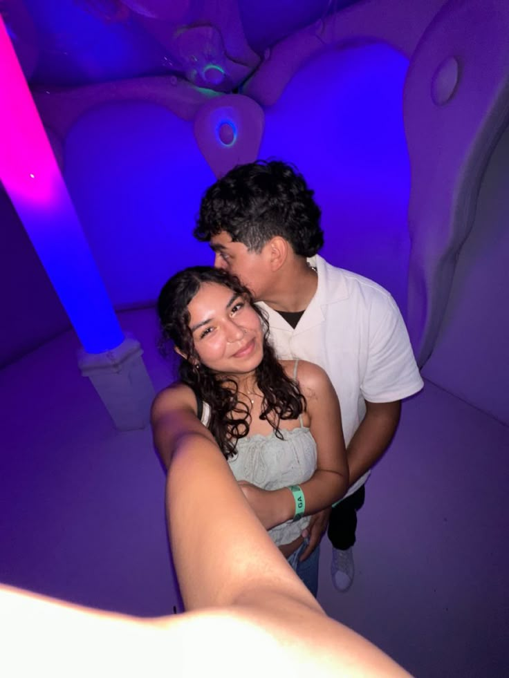 a man and woman are hugging in a room with blue lights on the walls behind them