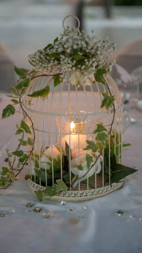 a white birdcage filled with candles and greenery on top of a table