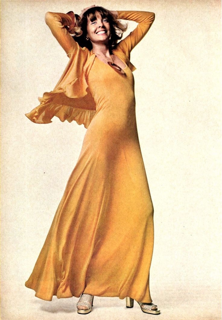 a woman in a long yellow dress is posing for the camera with her hands behind her head