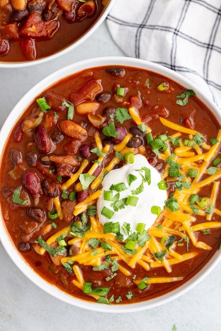 two bowls filled with chili, beans and cheese on top of a white tablecloth