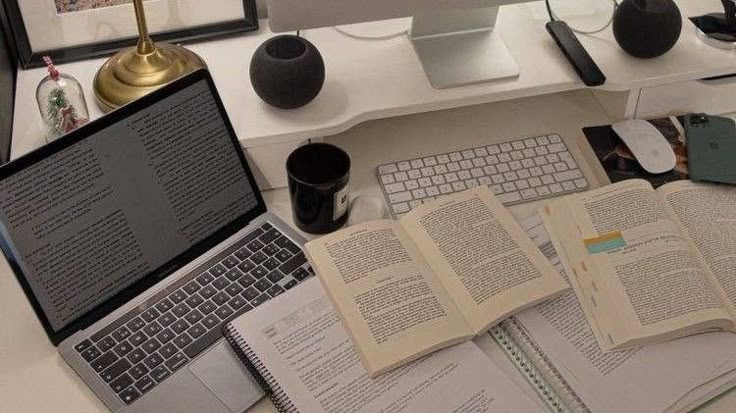 an open laptop computer sitting on top of a desk next to books and other items