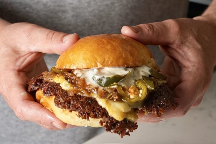 a person holding a hamburger with cheese and pickles on the bun in their hands