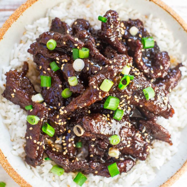 a white plate topped with meat and rice on top of a bed of green onions