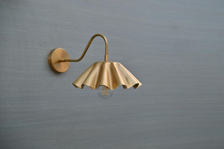 a brass wall light on the side of a gray wall with a white lamp shade