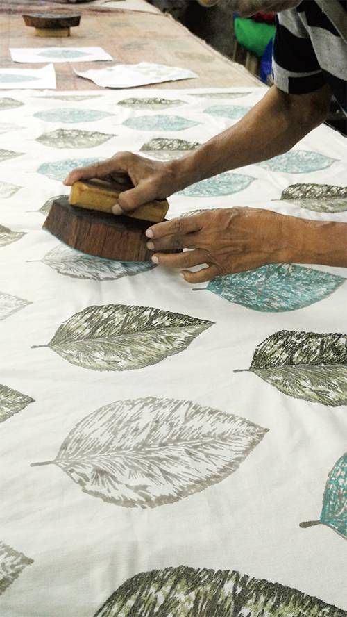 a woman is using a brush to paint leaves on a white tablecloth with blue and green designs