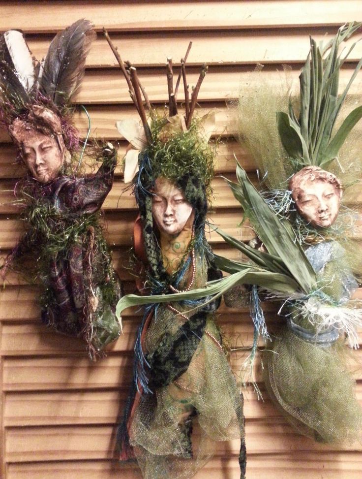 three dolls are hanging on the wall with plants in their hair and headdress