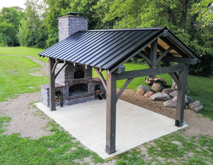 an outdoor fireplace with a metal roof in the middle of some grass and rocks on the ground