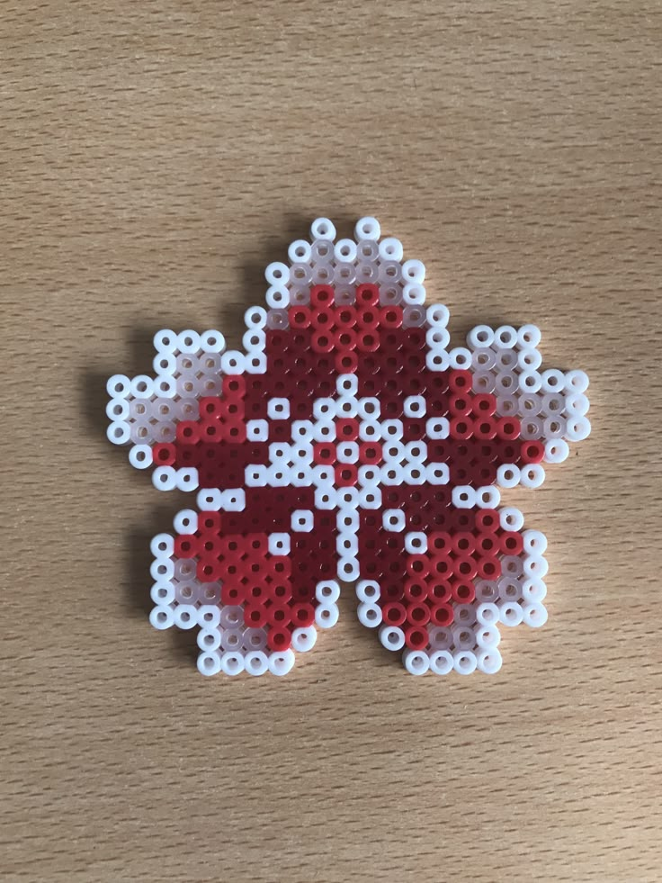 a red and white flower made out of perler beads on top of a wooden table