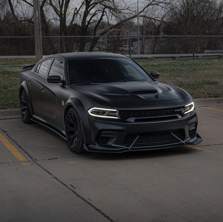 a black sports car parked in a parking lot next to a fence and some trees