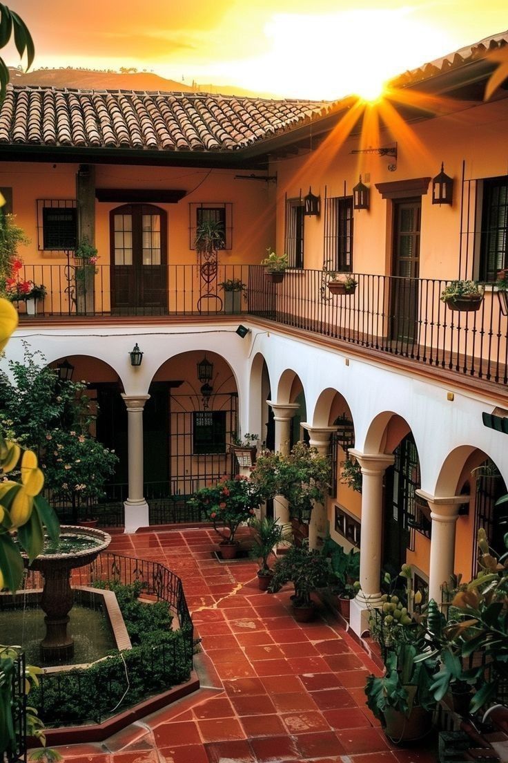 the sun is setting in front of an old building with courtyards and potted plants