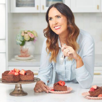 a woman sitting at a table with two cakes and strawberries on the plate in front of her