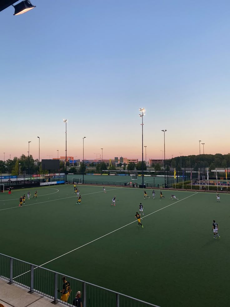 a group of people are playing soccer on a green field with lights in the background