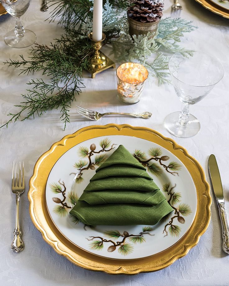 a christmas table setting with green napkins and gold plates