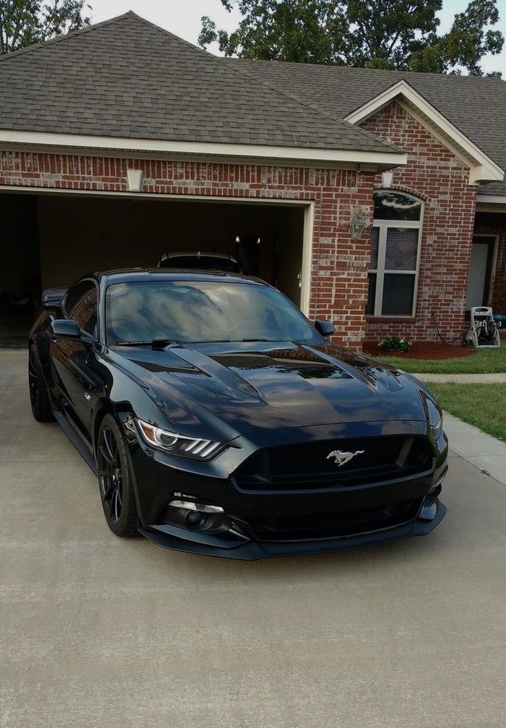 a black mustang parked in front of a brick house