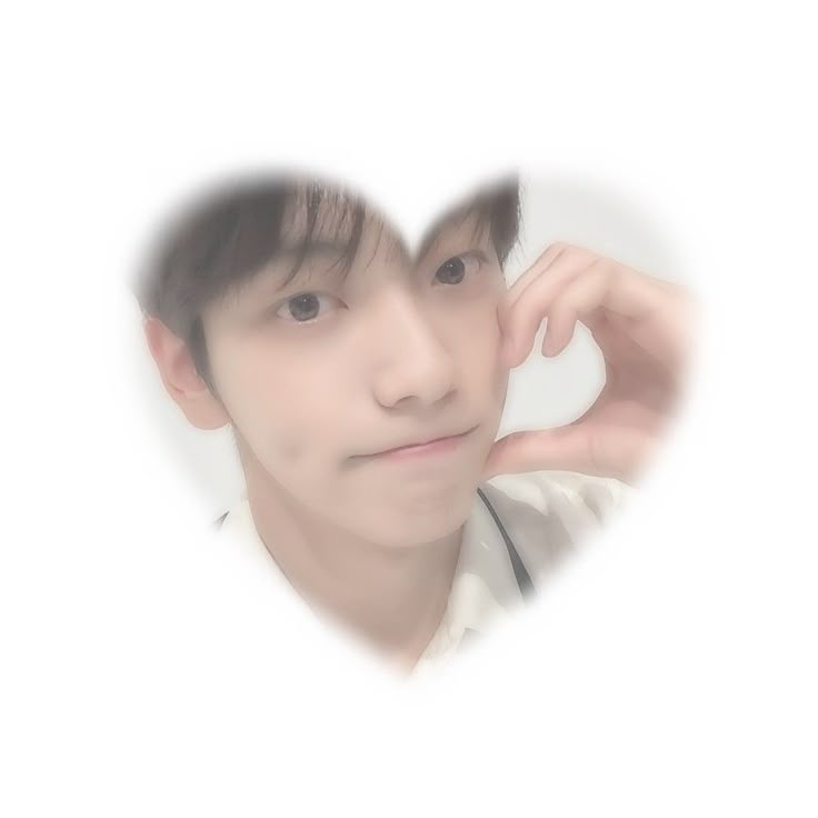 a young man is making a heart shape with his hand and looking at the camera