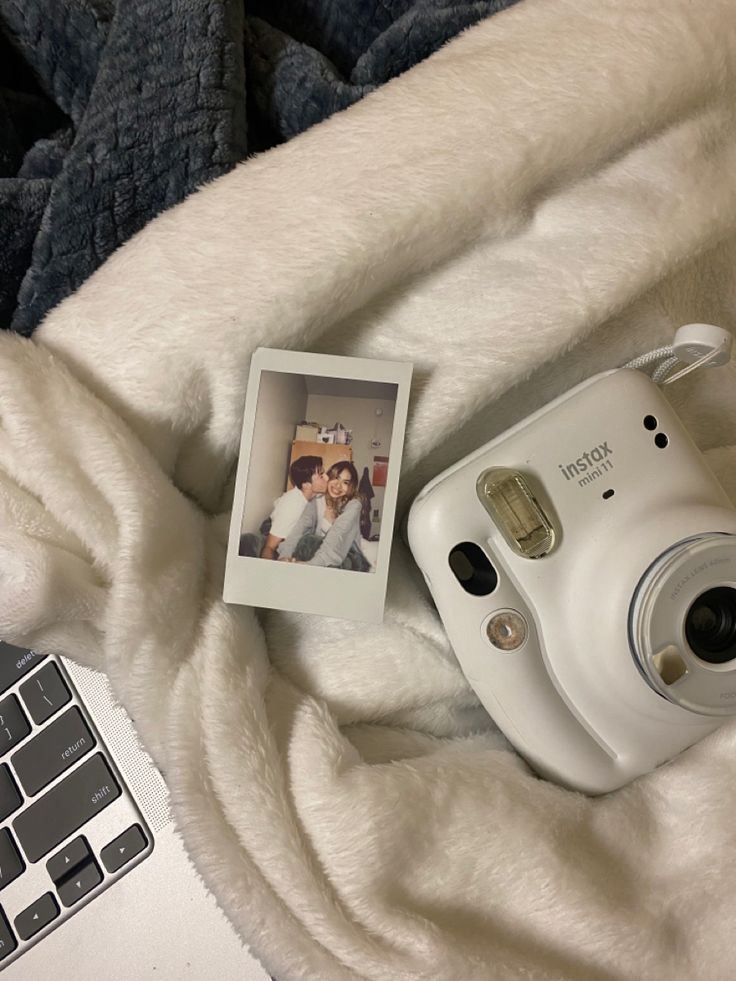 a polaroid camera sitting on top of a white blanket next to a laptop computer