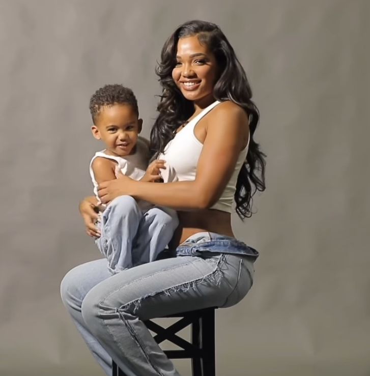 a woman sitting on top of a stool next to a boy with his arms around her