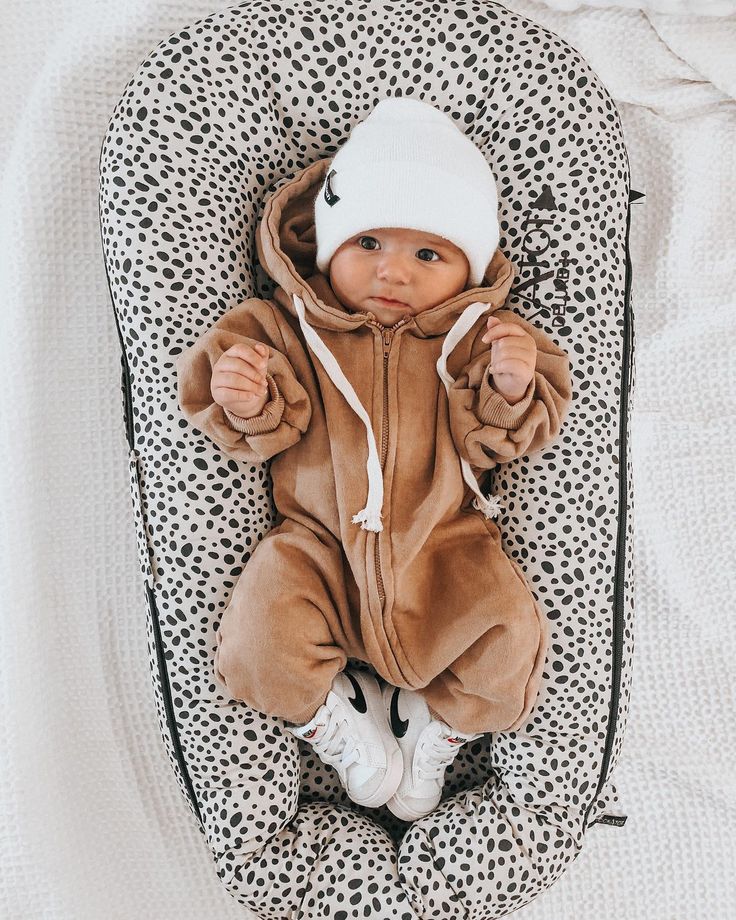 a baby in a brown bear costume laying on top of a white and black blanket