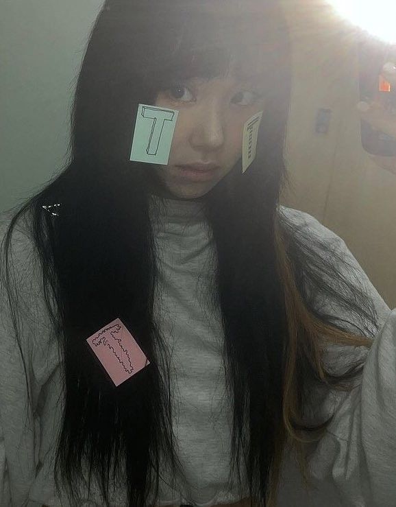 a woman with two sticky notes on her face and long black hair in front of a mirror