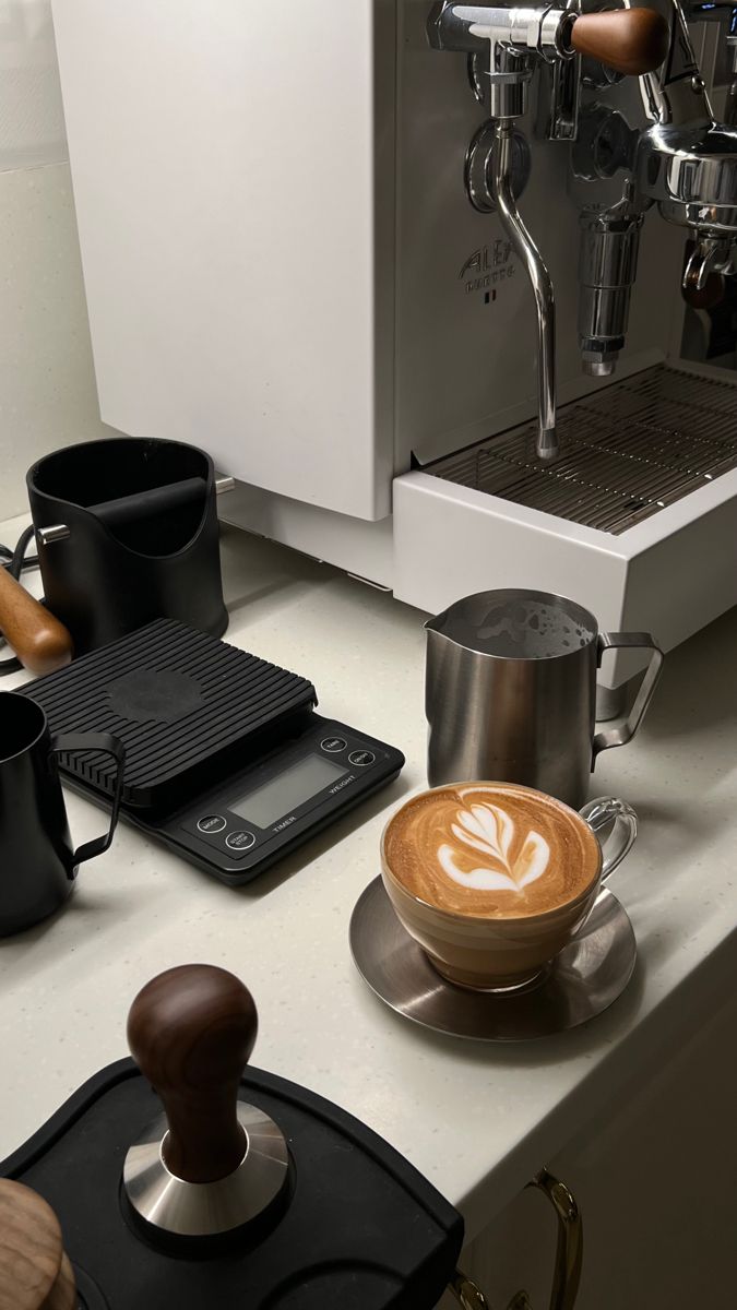 a cup of coffee sitting on top of a counter next to a grinder and some cups