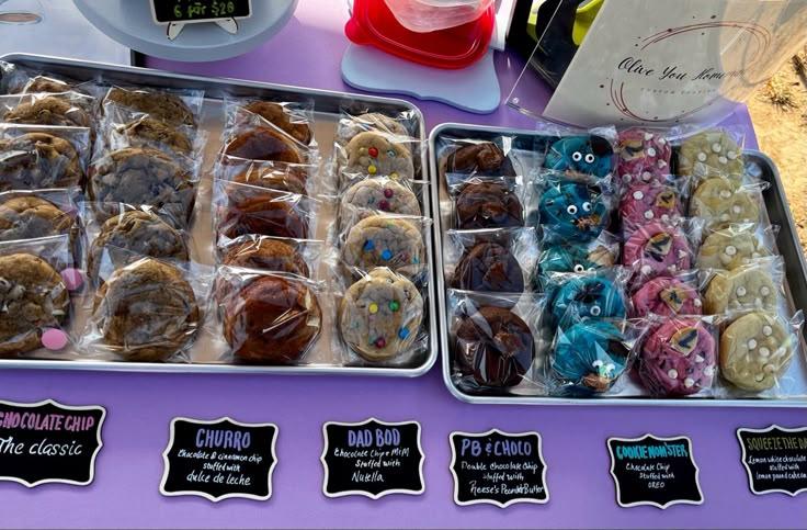 Cookies displayed at a farmers market on silver sheet pans in rows with chalkboard labels Bakers Market Stall, Baked Goods Market Stall, Easy Food Vendor Ideas, Cookies Farmers Market, Baked Goods Vendor Booth, Cookie Popup Display, Dessert Farmers Market, Snacks To Sell At Farmers Market, Baking For Markets