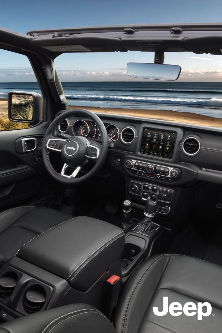 the interior of a jeep with black leather seats and steering wheel, looking out at the ocean