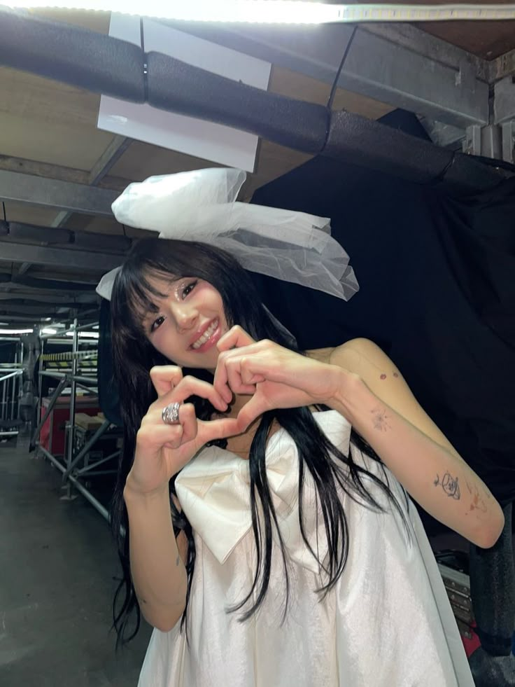 a woman in a white dress making a heart with her hands