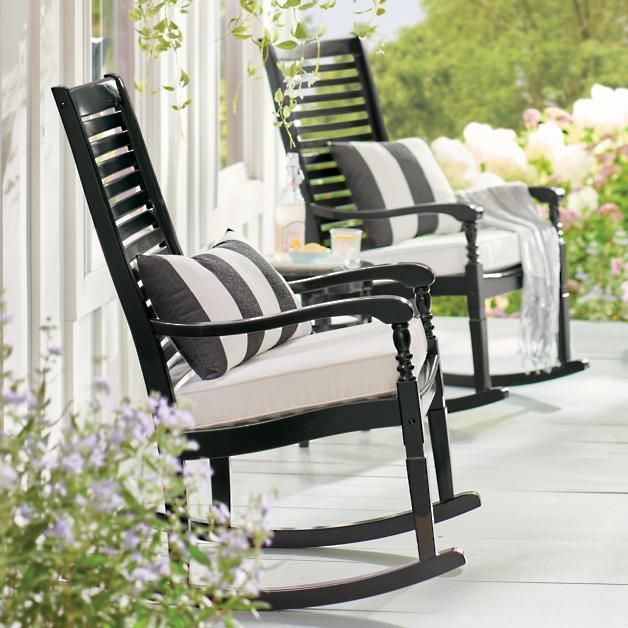 black and white rocking chairs sitting on a porch with flowers in the vases next to them