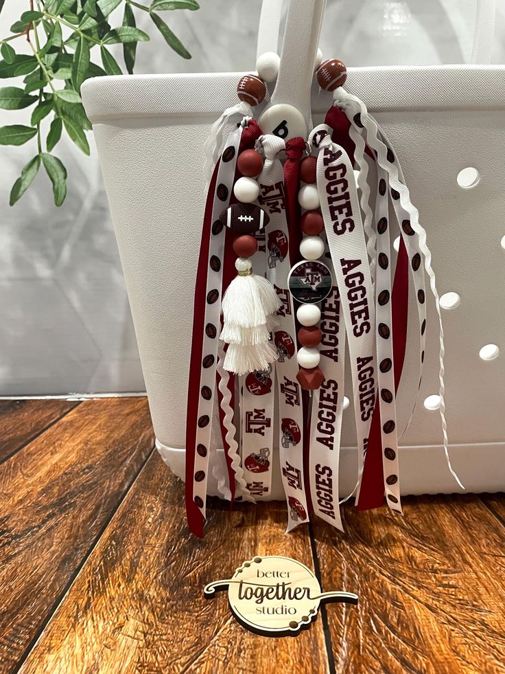 a white bag with red and white beads hanging from it's side on a wooden table