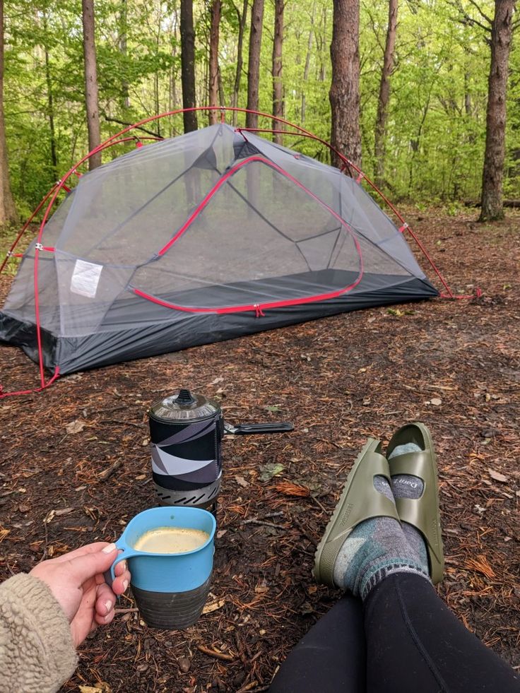 a person sitting in front of a tent with a cup of coffee next to it