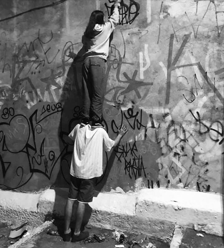 two people standing in front of a wall with graffiti on it