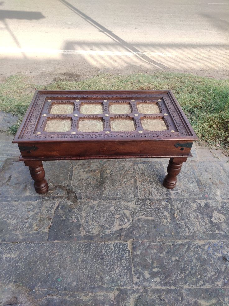 an old wooden table sitting on top of a stone floor next to a grass covered sidewalk