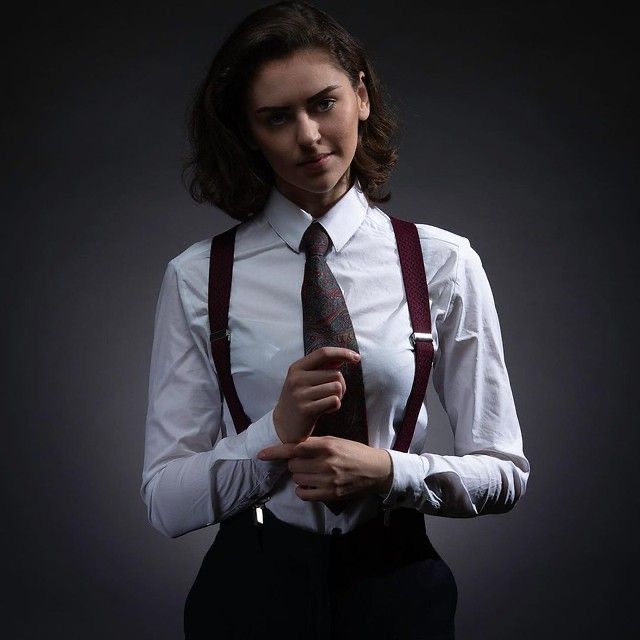 a woman wearing suspenders and a white shirt is holding a tie in her hands