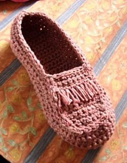 a pair of crocheted slippers sitting on top of a bed next to a flower