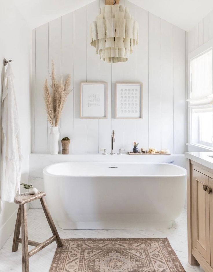 a white bath tub sitting in a bathroom next to a wooden stool and sink under a chandelier