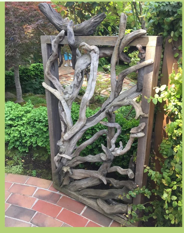 a wooden frame made out of driftwood in a garden with brick walkway and shrubbery