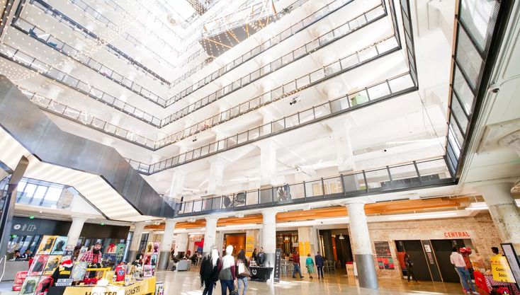 people are walking around in the lobby of an office building with high ceilings and glass balconies