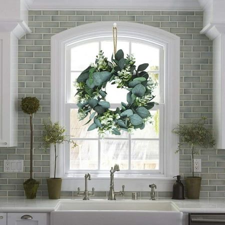 a wreath is hung on the window sill above a sink in a white kitchen